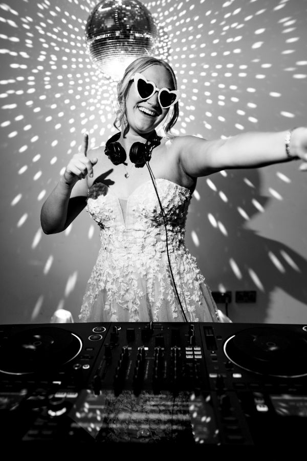 Bride DJing under a disco ball in heart sunglasses