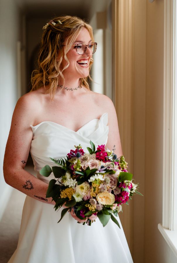 Bride in glasses laughing by a window while getting ready