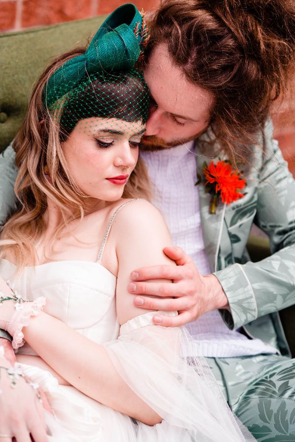 Bride in a green birdcage veil leaning on her partner