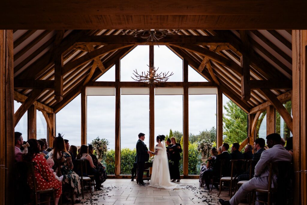Ceremony under oak beams with a wall of windows