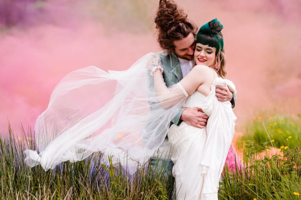 Couple embracing in a meadow with pink smoke and a flowing veil